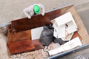 bricklayer mason worker depositing furniture and tiles in rubble dumpster container in Baltimore City