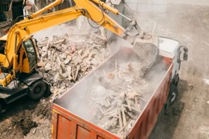 excavator breaks building and loads construction waste into truck with its bucket