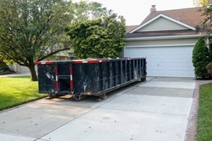 long blue dumpster full of wood and other debris in the driveway in front of a house in the suburbs that is being renovated